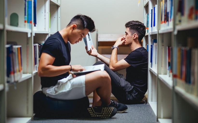 The photo shows 2 students in a library.